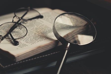 a magnifying glass sits atop a book alongside a pair of glasses