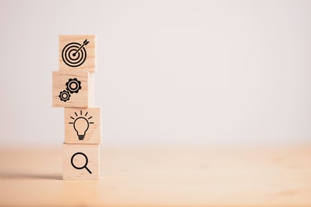 wooden blocks stacked with target, gears, light bulb, and magnifying glass