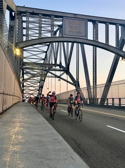 bikers riding across a bridge at sunrise
