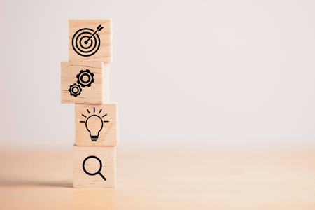 four blocks with target, gears, light bulb, and magnifying glass