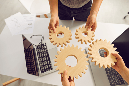 hands holding gears with laptops in the background